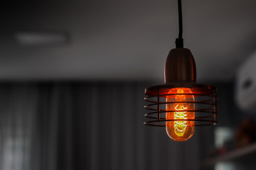 Close-up of an illuminated vintage Edison bulb casting a warm glow in a contemporary room setting.